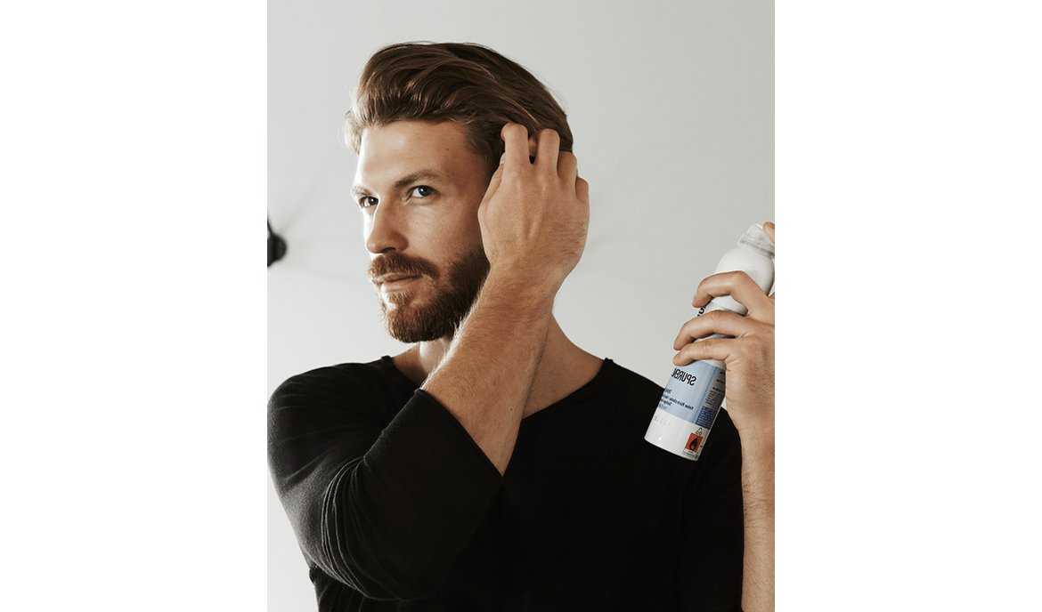 Bärtiger Mann mit braunem Haar stylt sich mit Haarspray